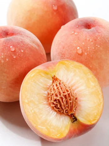 Pêssegos inteiros e fatiados em mesa de madeira, ao lado de copo de sumo