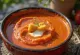 Sopa de tomate cremosa com cor avermelhada, servida em prato branco